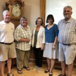 Two men and three women standing in front of a granfather clock and windows"